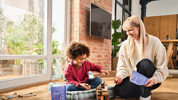 A woman and a child sitting together by a window while playing, with the woman holding a Mondi package.